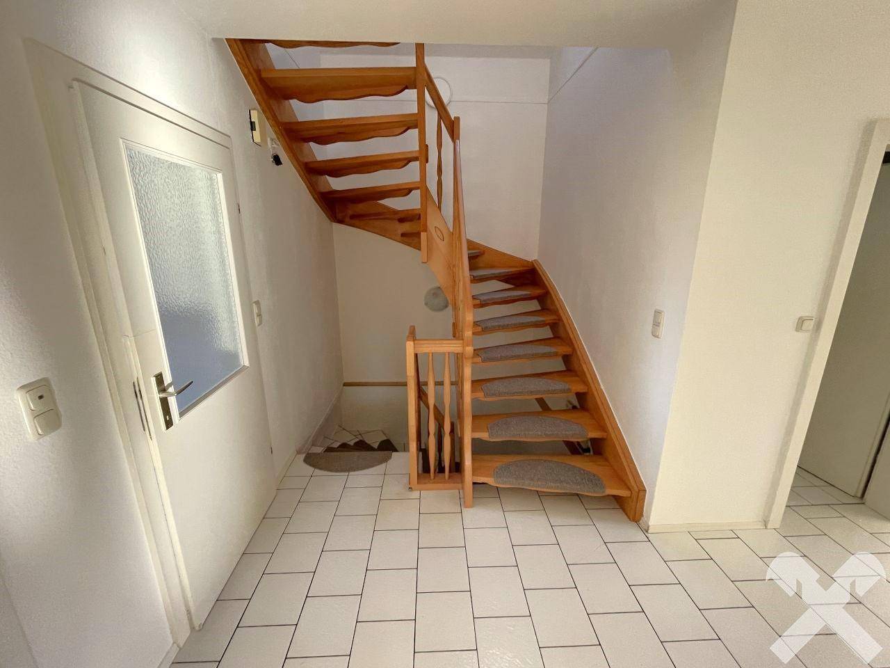 Geräumiger Flur mit Holztreppe zum Obergeschoss und hellem Fliesenboden.