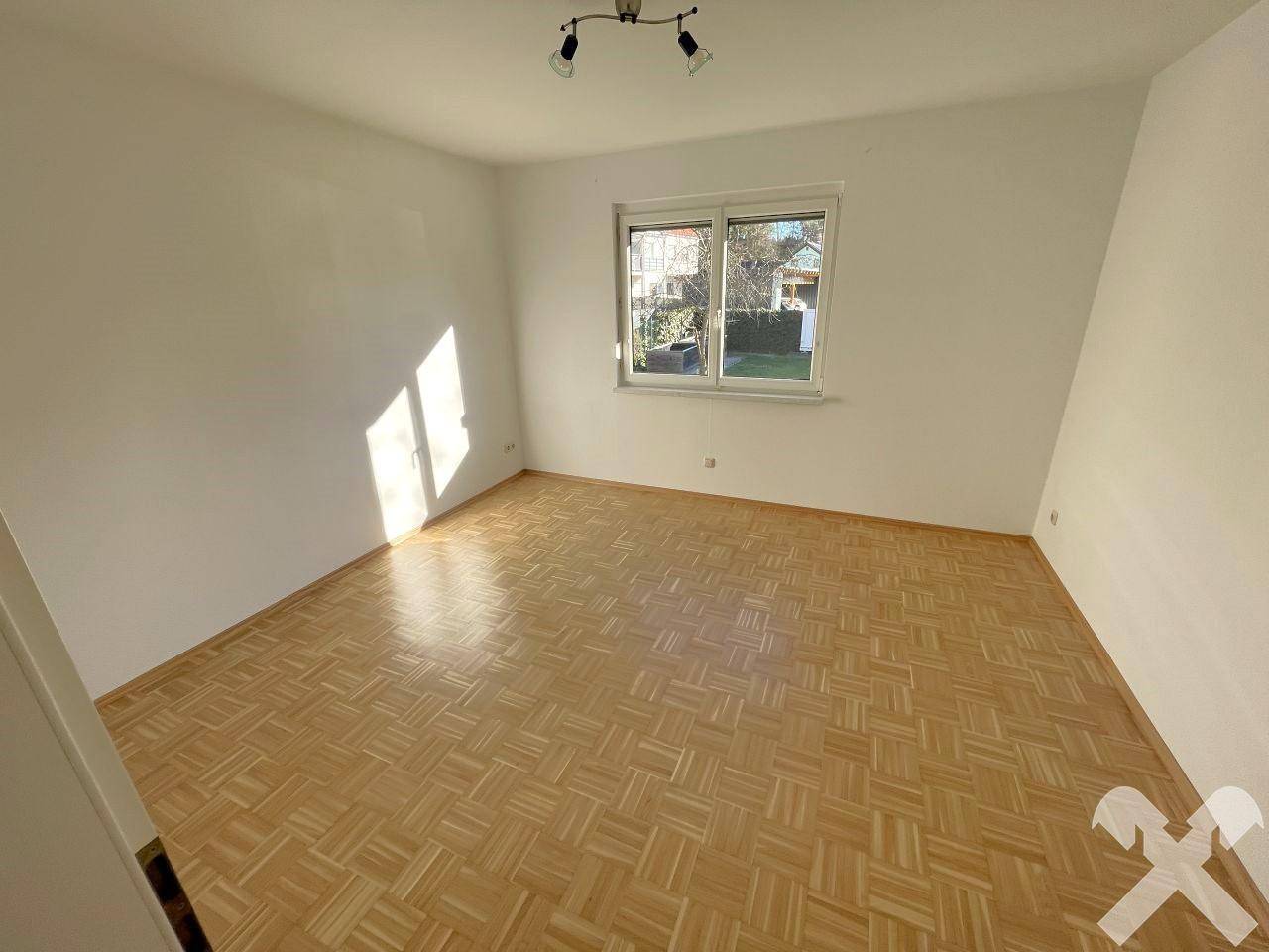 Helles Schlafzimmer mit Parkettboden und großem Fenster, bietet viel Tageslicht.