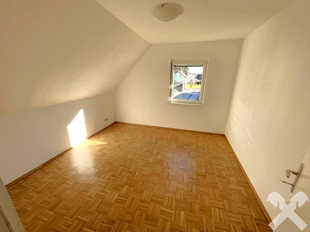 Helles Schlafzimmer im Dachgeschoss mit Parkettboden und Fenster, bietet viel Tageslicht.