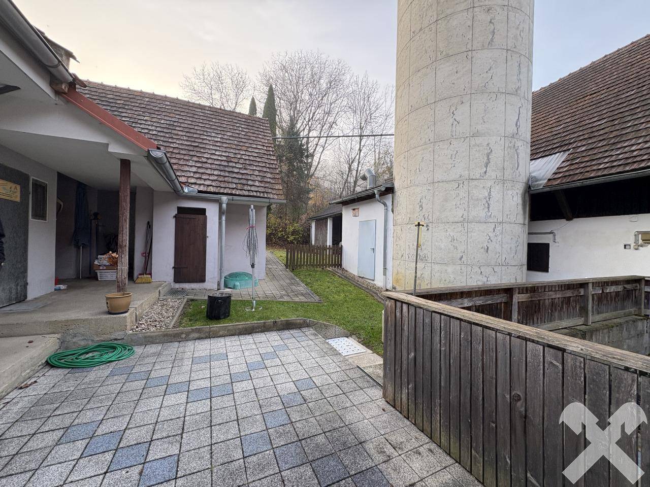 Weitläufiger gepflasterter Bereich mit angrenzendem Rasen und einem hohen Silo im Hintergrund.