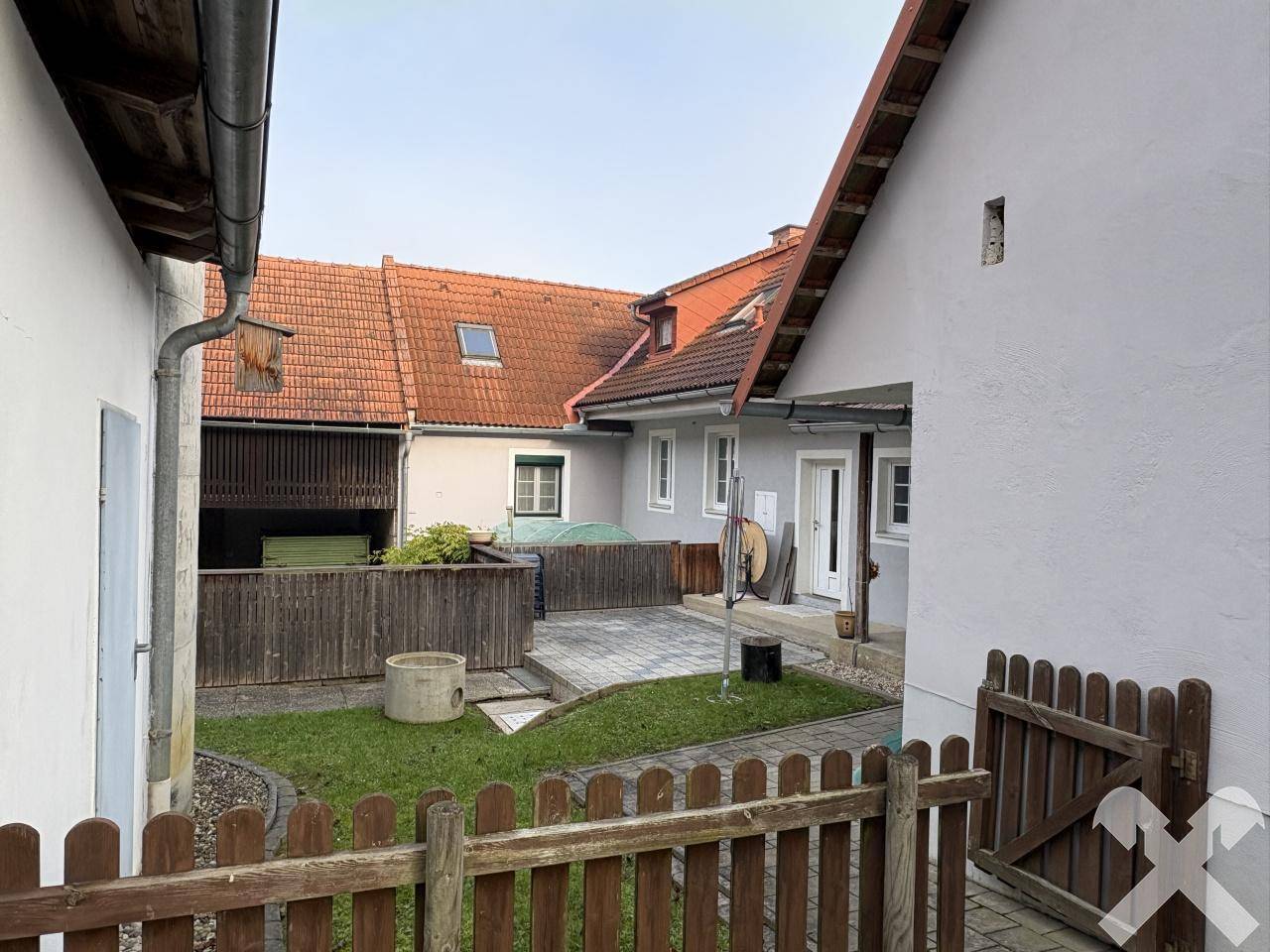 Kleiner Innenhof mit gepflastertem Bereich, Rasenfläche und Holzzaun zwischen den Gebäuden.
