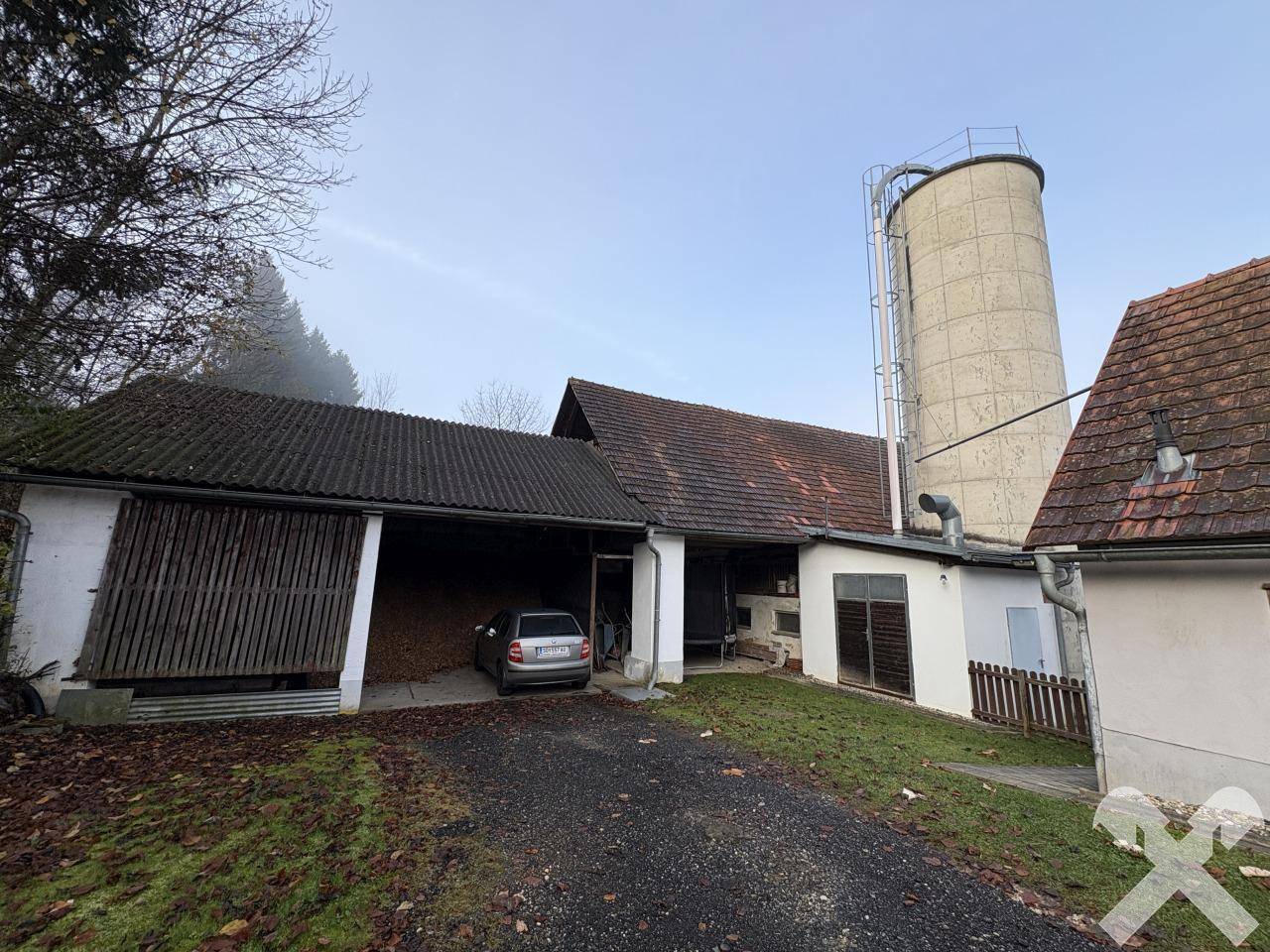 Mehrere Wirtschaftsgebäude mit Silo und einem überdachten Stellplatz für ein Fahrzeug.
