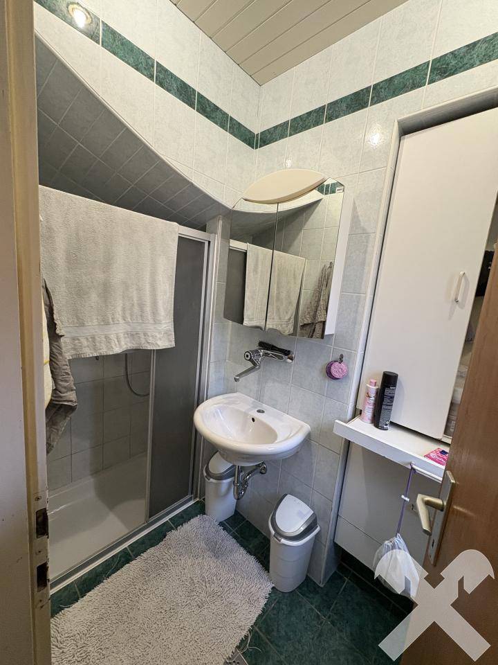 Badezimmer mit grünen und weißen Fliesen, Dusche, Waschbecken und Spiegelschrank.