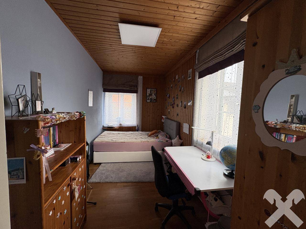 Kinderzimmer mit Holzvertäfelung, Einzelbett und Schreibtisch am Fenster.