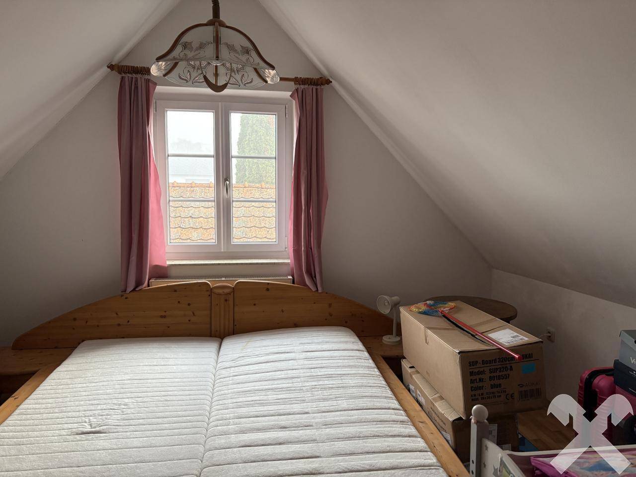 Gemütliches Schlafzimmer im Dachgeschoss mit Holzbett und Fenster mit Blick auf die Dächer.