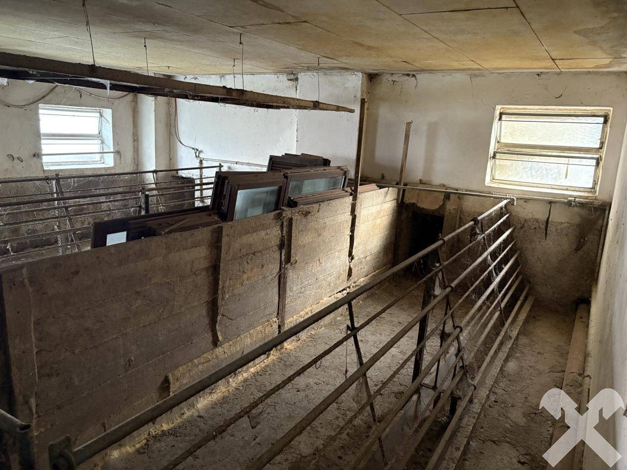 Alter Stallraum mit Holztrennwänden und kleinen Fenstern, der Renovierung bedarf.