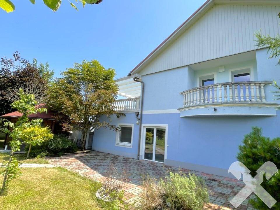 Seitenansicht des Gebäudes mit Balkon, gepflastertem Bereich und Grünflächen.