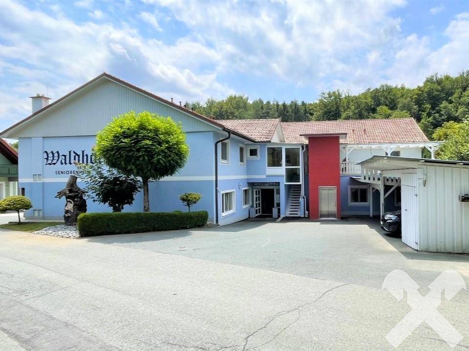 Vorderansicht des Gebäudes mit blauer Fassade, externem Aufzug und umgebender Natur.