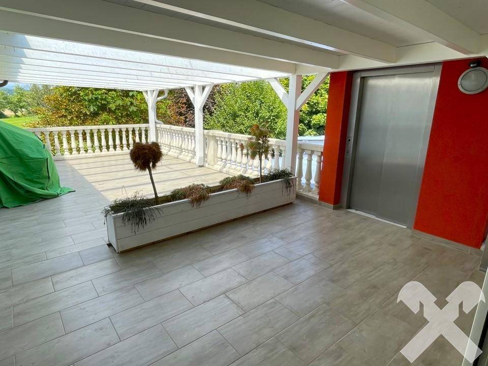 Große überdachte Terrasse mit Fliesenboden, Balustrade und externem Aufzug.