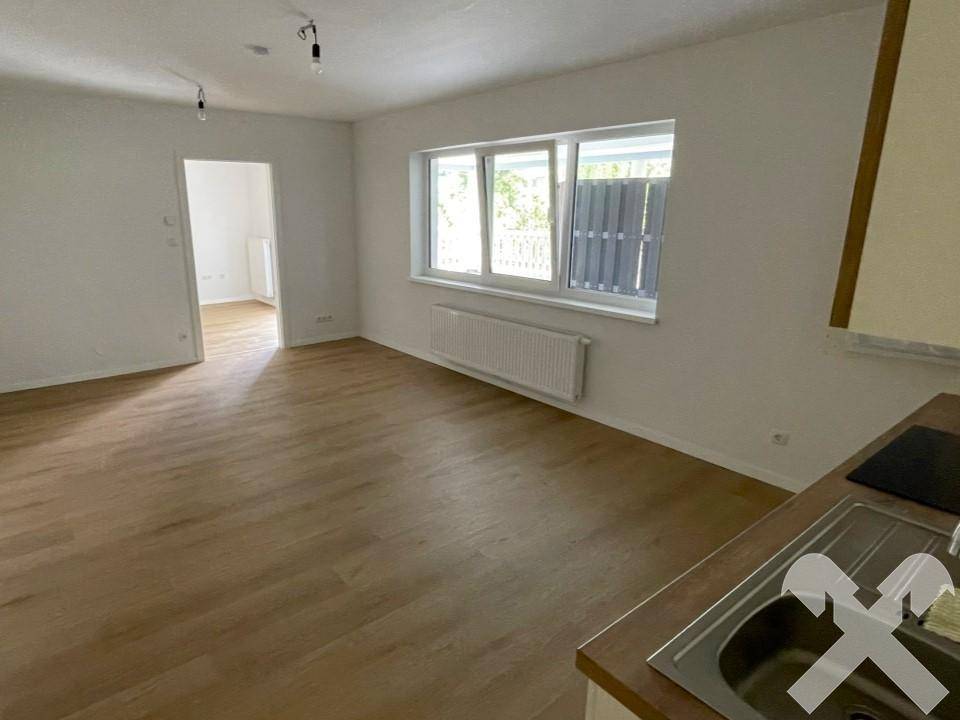 Heller Wohnbereich mit Laminatboden, großen Fenstern und integrierter Küchenzeile.