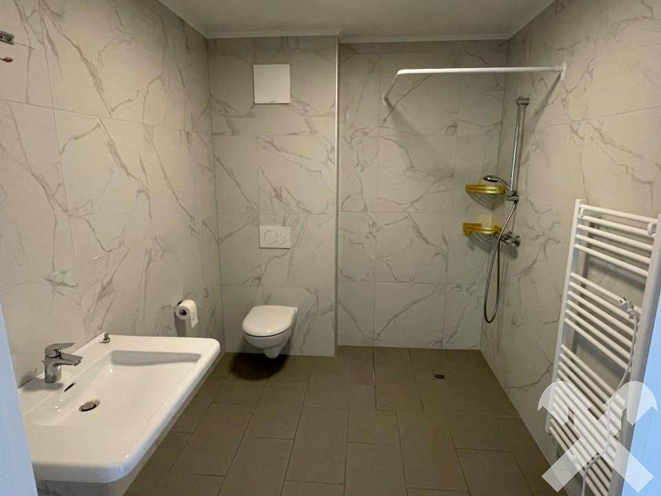 Modernes Badezimmer mit großformatigen Fliesen, ebenerdiger Dusche und beheiztem Handtuchhalter.