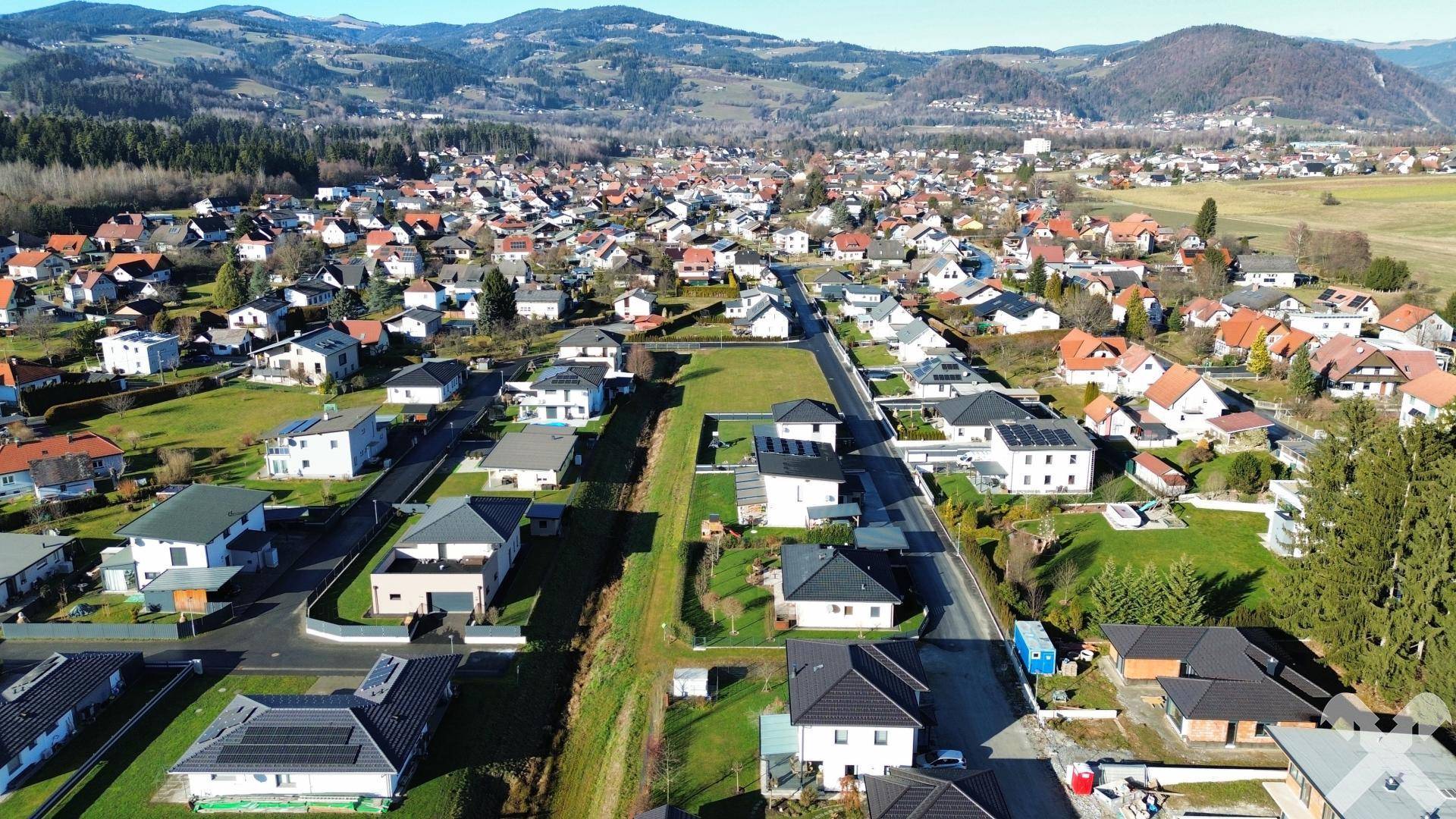 Luftaufnahme einer Wohnsiedlung mit vielen Einfamilienhäusern und bergiger Landschaft im Hintergrund.