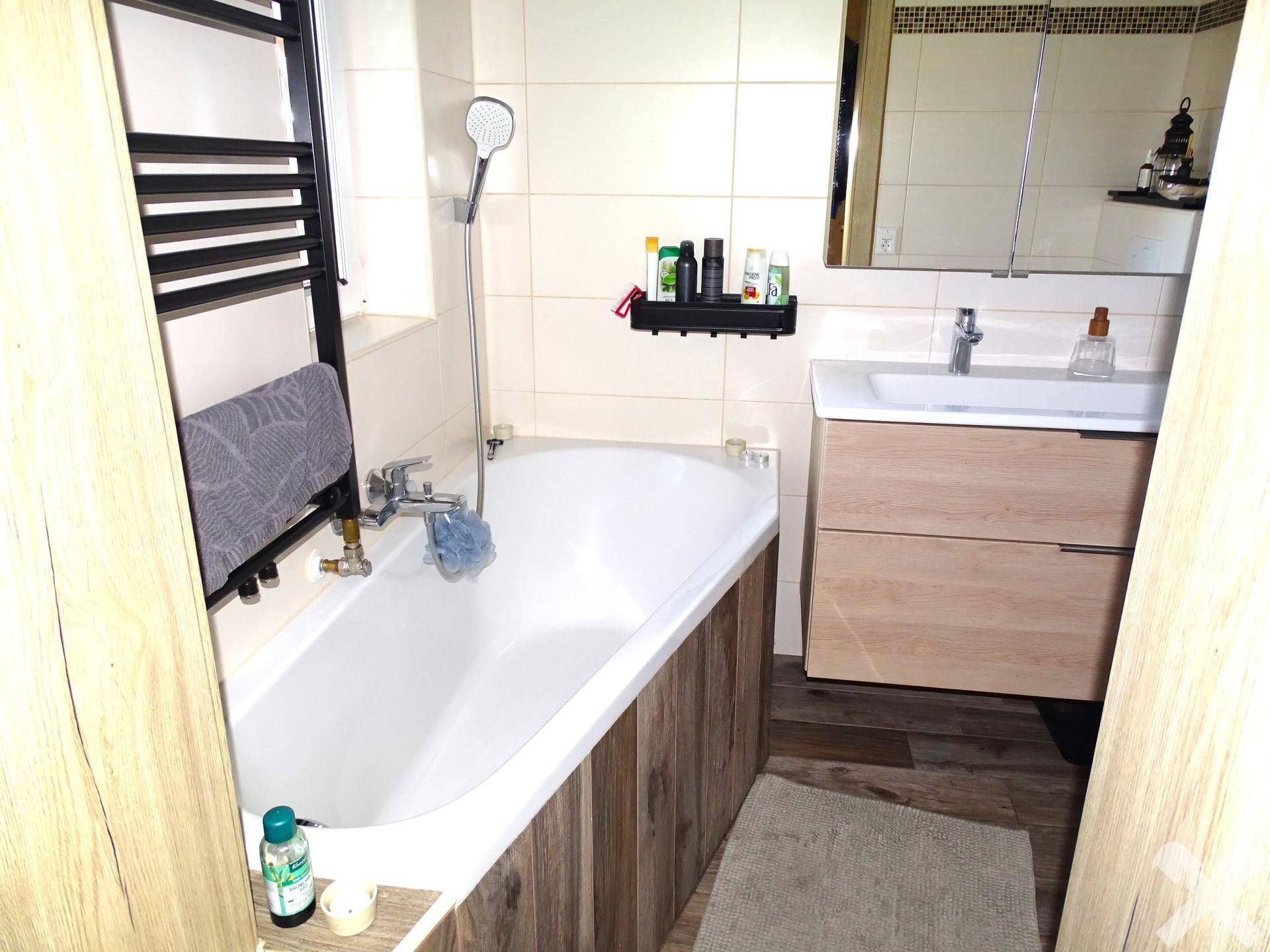 Funktionales Badezimmer mit Badewanne, beheiztem Handtuchhalter und Holzoptik-Fliesen.