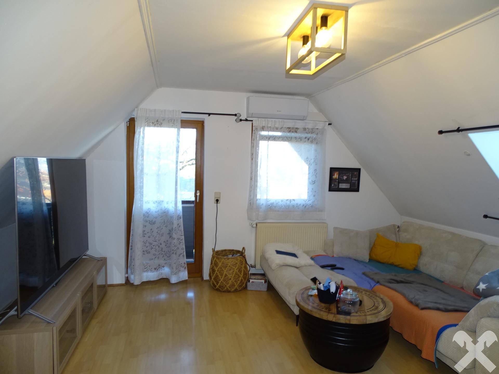 Gemütliches Wohnzimmer im Dachgeschoss mit Schrägen, Holzboden und Klimaanlage.