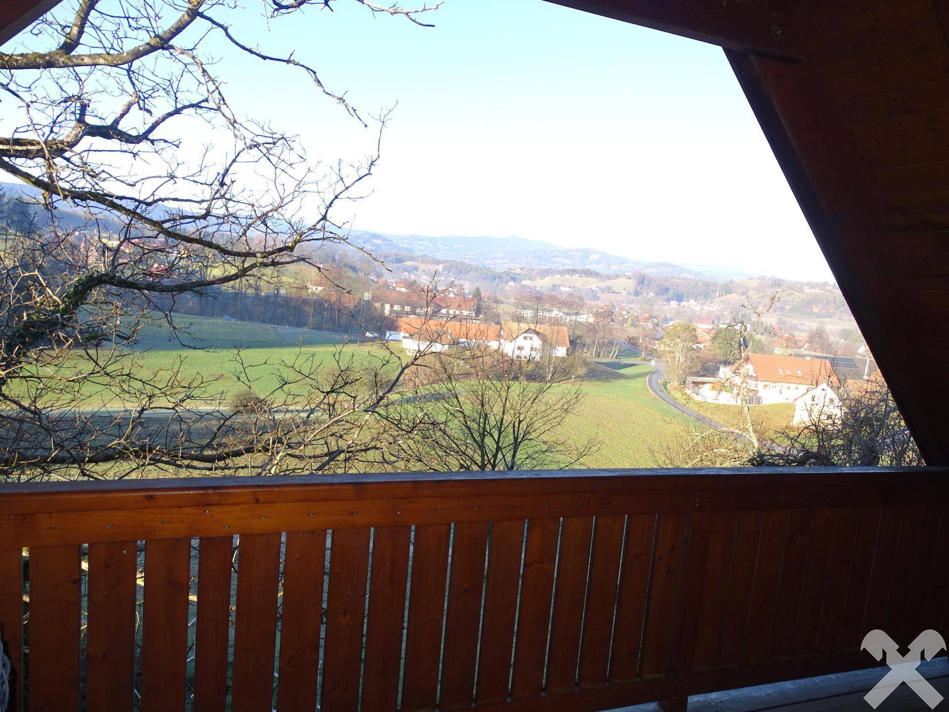Überdachte Loggia mit weitem Blick über die grüne Landschaft und umliegende Häuser.
