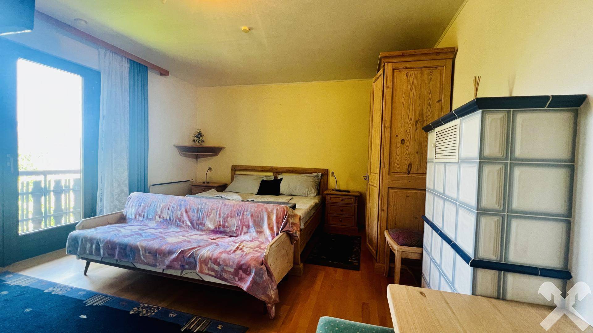 Schlafzimmer mit Kachelofen, Sofa und direktem Zugang zu einem Balkon.