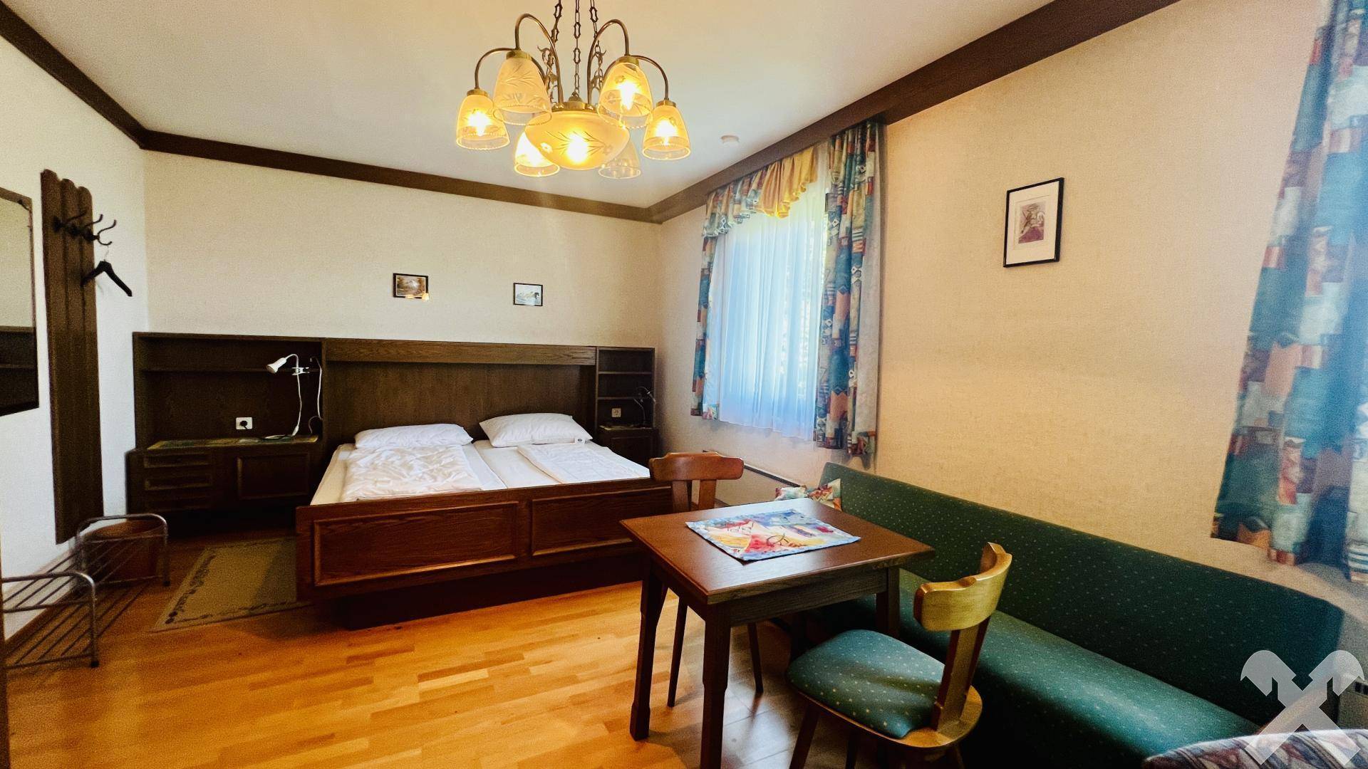 Schlafzimmer mit Doppelbett, kleinem Esstisch und traditioneller Einrichtung.