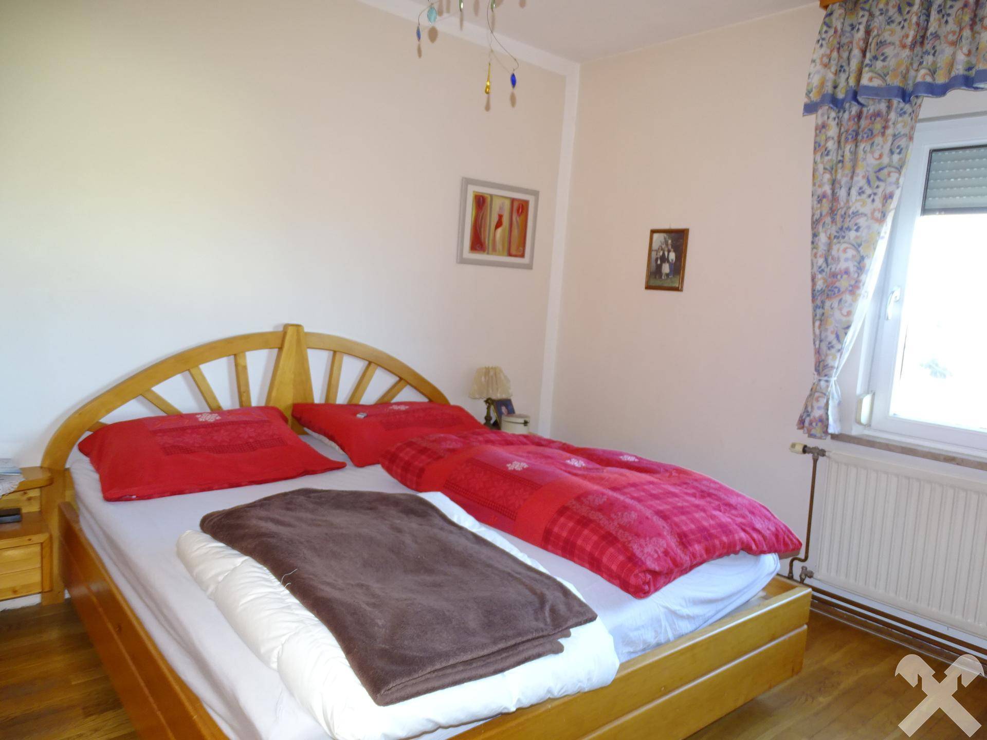 Helles Schlafzimmer mit Doppelbett, Holzmöbeln und Fenster mit Blick ins Grüne.