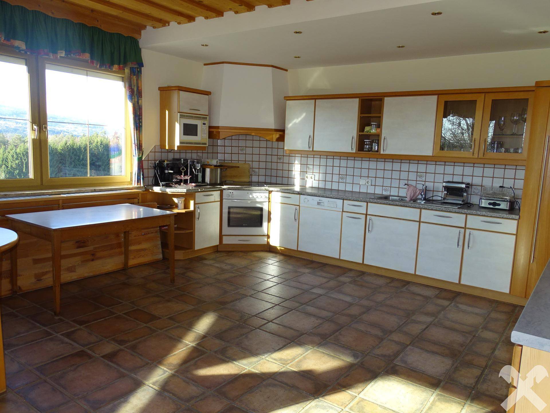 Geräumige Wohnküche mit Terrakotta-Fliesenboden, Holzschränken und großem Fenster mit Weitblick.