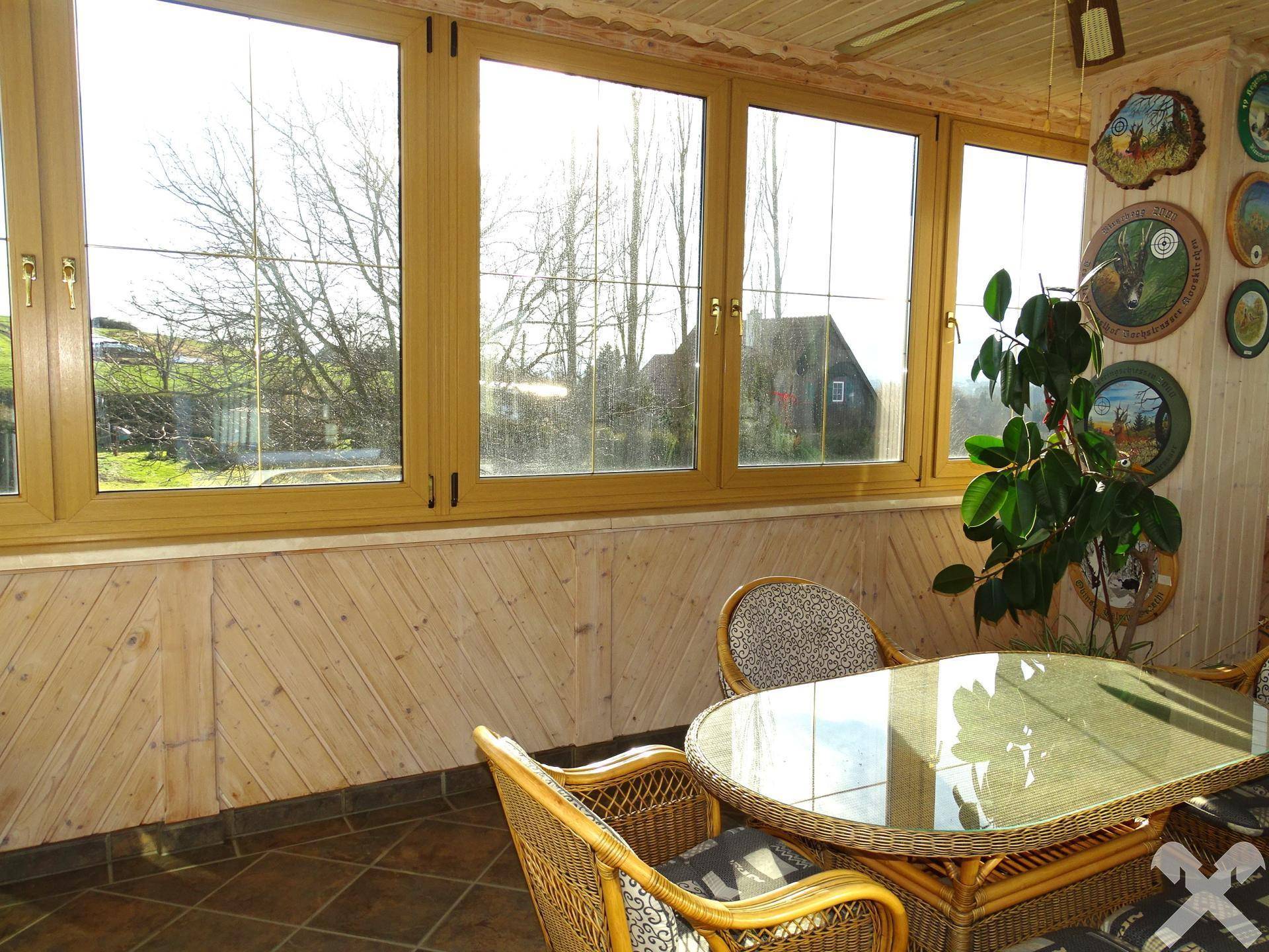 Heller Wintergarten mit großen Fenstern, Rattanmöbeln und Holzverkleidung, ideal zum Entspannen.