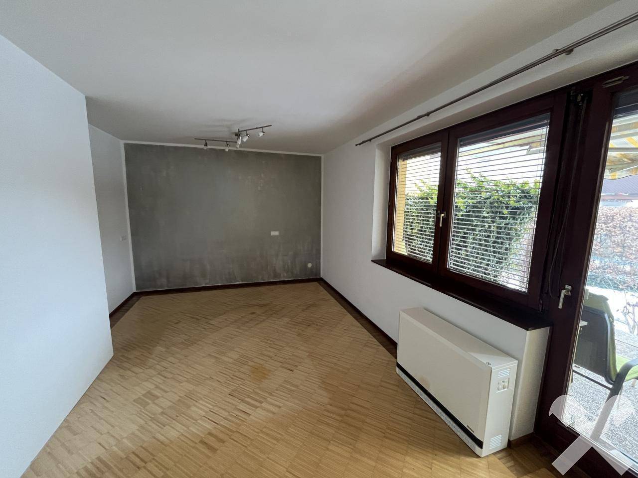 Wohnzimmer mit Parkettboden, einer Akzentwand und großen Fenstern.