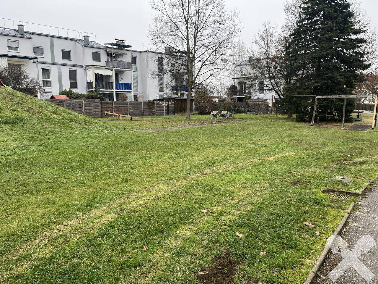 Gemeinschaftlicher Spielplatz mit Schaukeln und Wippe, umgeben von Grünflächen.