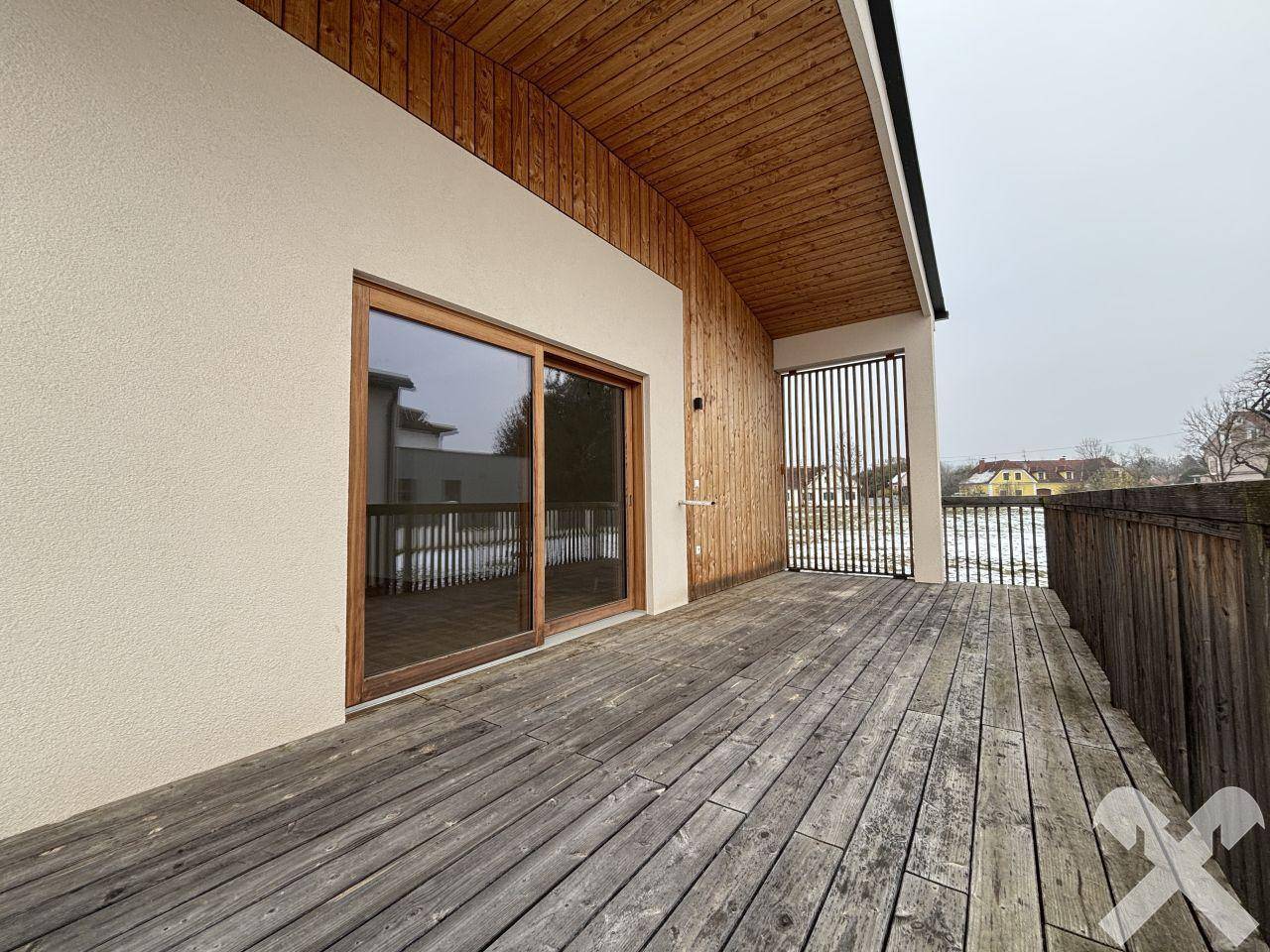 Geräumige Holzterrasse mit Schiebetür zum Innenbereich und Blick auf die Umgebung.