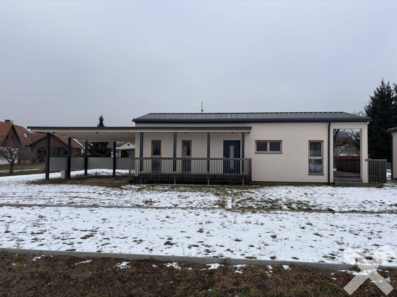 Gesamtansicht des modernen Einfamilienhauses mit Carport und weitläufiger Holzterrasse im Winter.