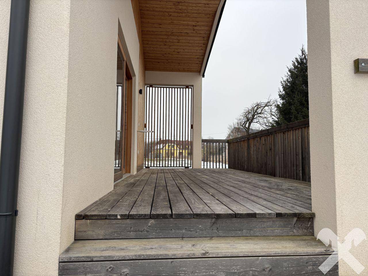 Holzterrasse mit Stufen und Geländer, die zum Eingang des modernen Hauses führen.