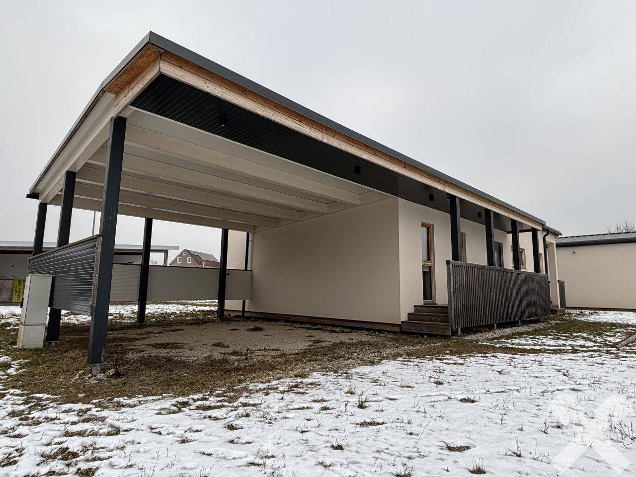 Seitliche Ansicht des Hauses mit überdachtem Carport und angrenzender Terrasse.