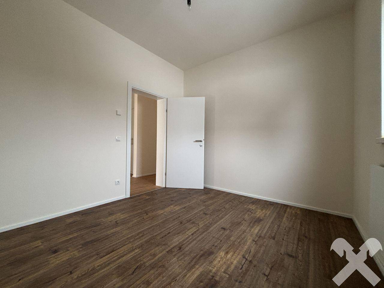 Helles Zimmer mit Laminatboden und Fenster, das viel Tageslicht hereinlässt.