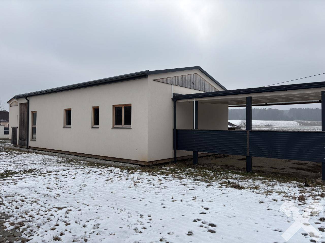 Längsseite des Hauses mit Carport-Anbau und Blick auf die verschneite Landschaft.