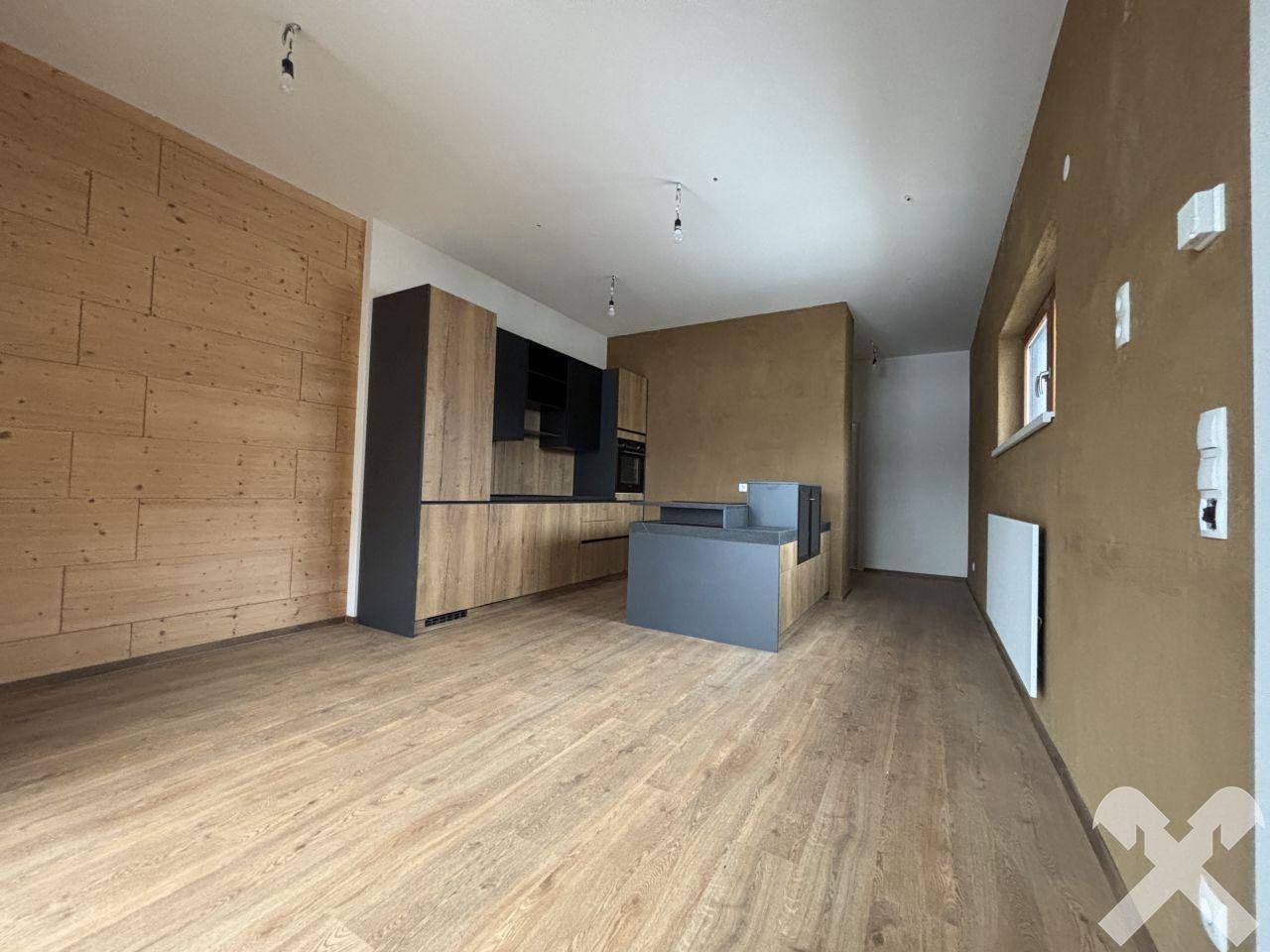 Offener Wohn- und Küchenbereich mit Holzwand und modernem Design, ideal für geselliges Beisammensein.