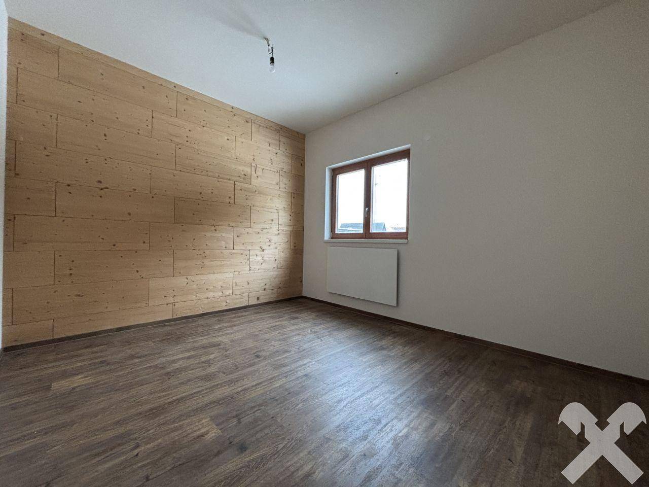 Helles Zimmer mit Holzwand und Fenster für natürliches Licht, ausgestattet mit Holzboden.