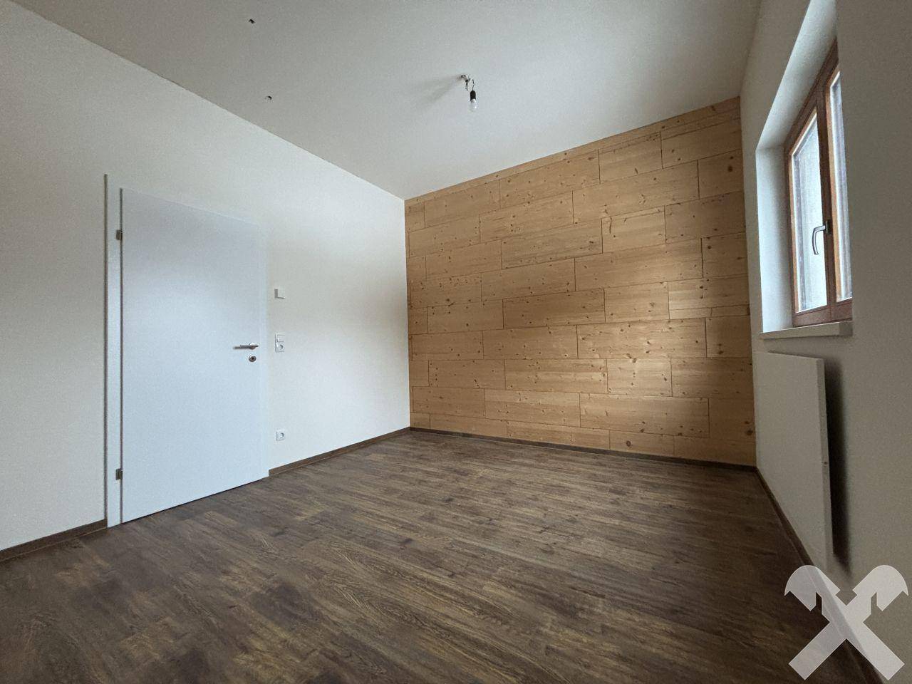 Geräumiges Zimmer mit Holzwand, Holzboden und weißer Tür, bereit zur individuellen Gestaltung.