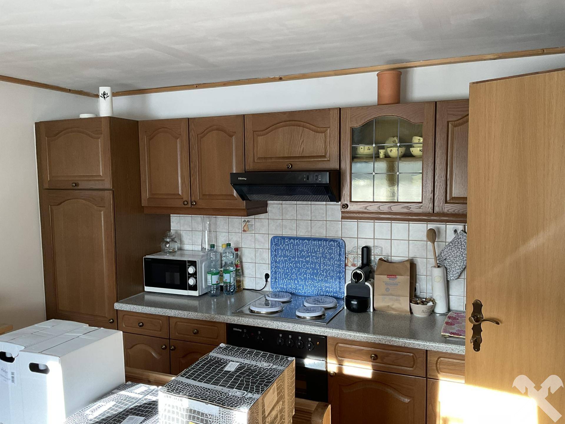 Funktionale Küche mit Holzschränken, Fliesenrückwand und grundlegenden Küchengeräten.
