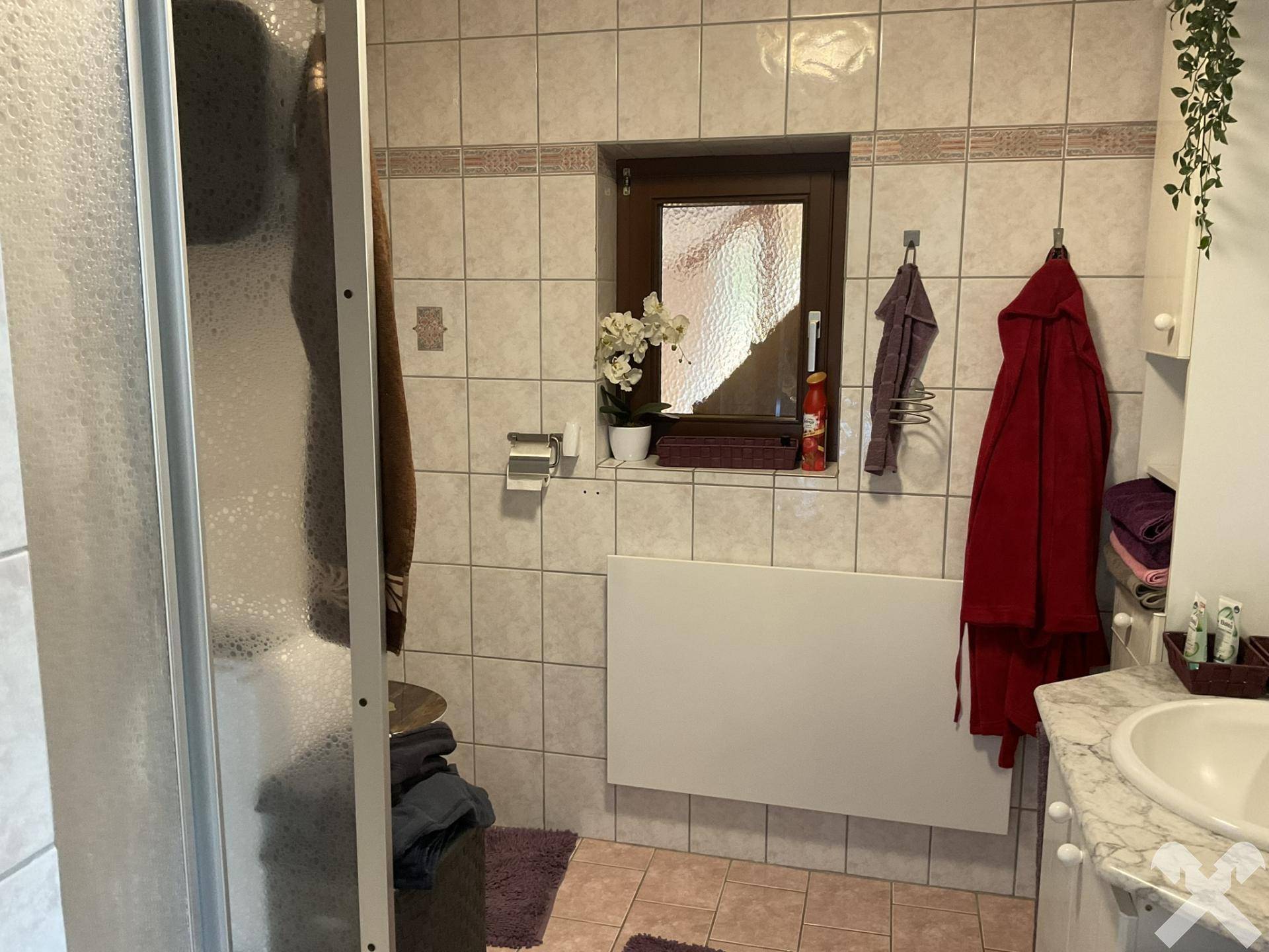 Gefliestes Badezimmer mit Dusche, Fenster und Heizkörper, in traditionellem Stil gehalten.