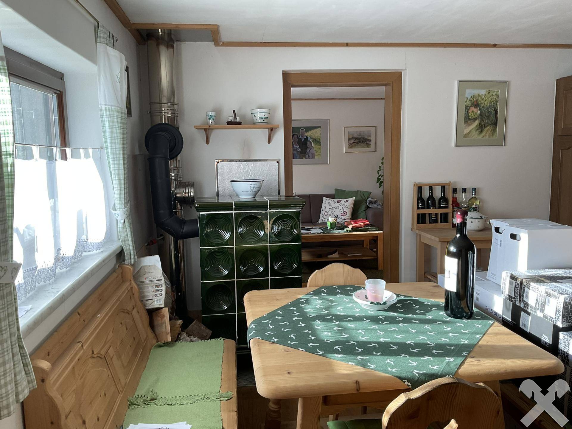 Essbereich mit traditionellem Kachelofen, Holzbänken und Blick in ein weiteres Zimmer.