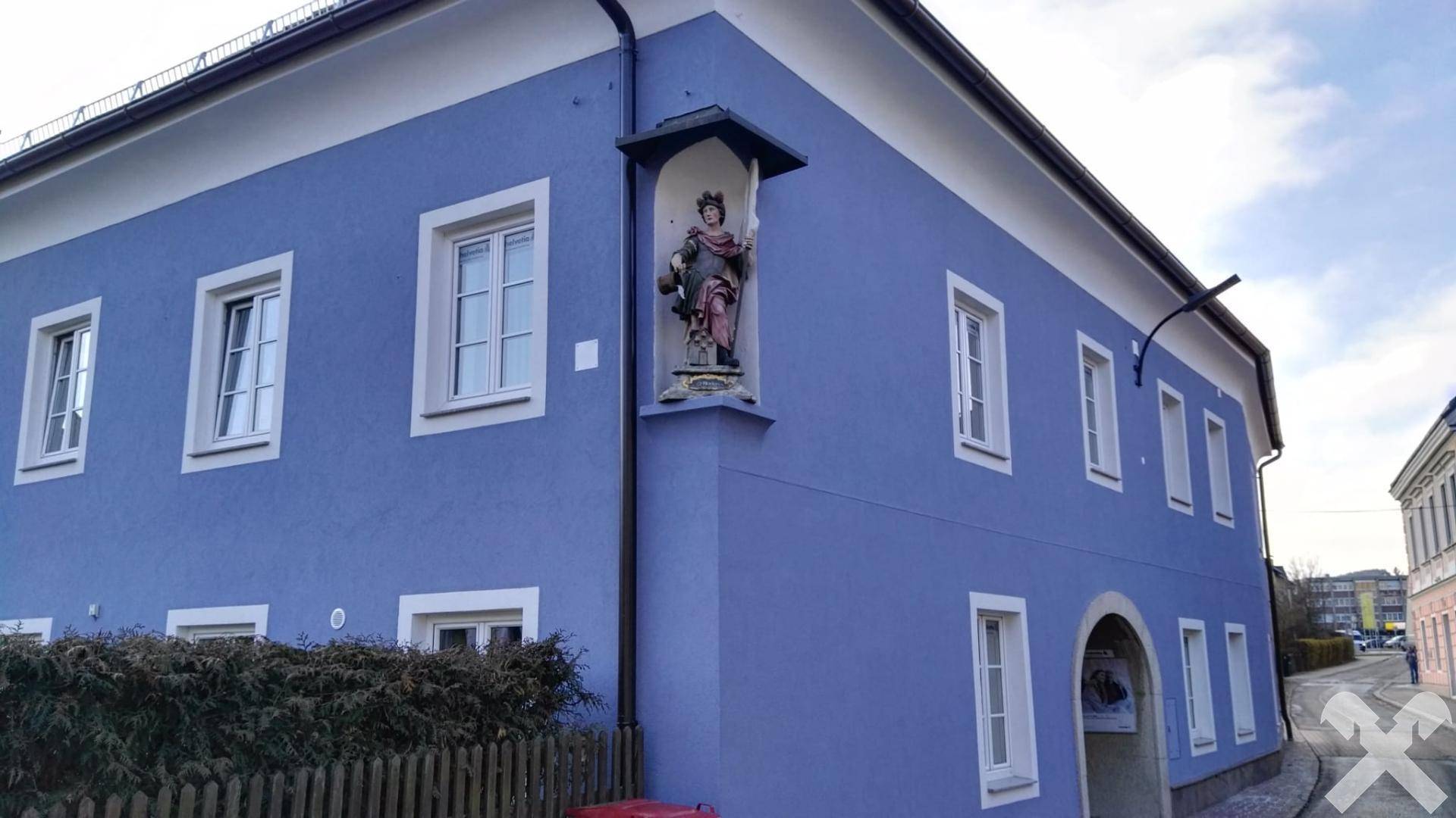 Nahaufnahme der blauen Fassade mit einer Nische, die eine Statue beherbergt, und weißen Fenstern.