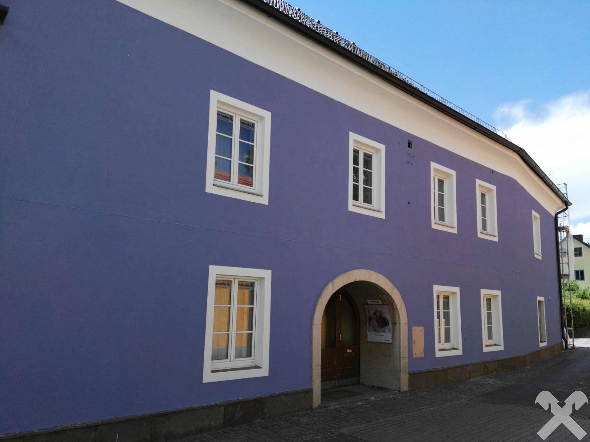 Lange blaue Fassade des Gebäudes mit einem gewölbten Eingang und mehreren weißen Fenstern.