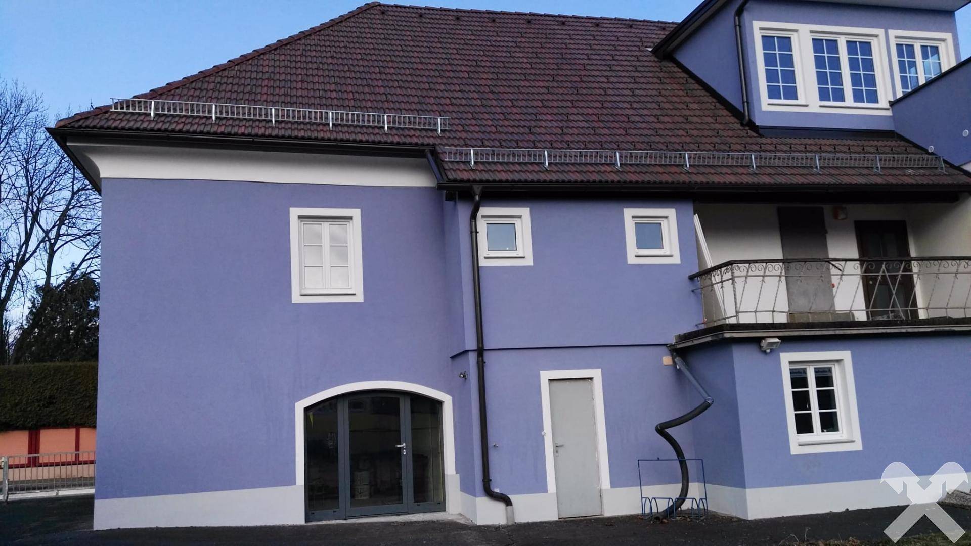 Rückseite des Gebäudes mit einem Balkon, großen Fenstern und einem Satteldach.