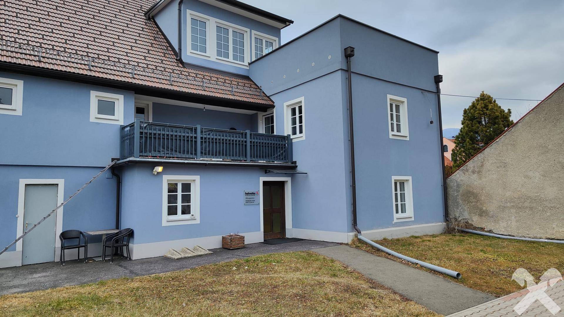 Rückansicht des blauen Gebäudes mit Balkon, Rasenfläche und einem angrenzenden Nebengebäude.