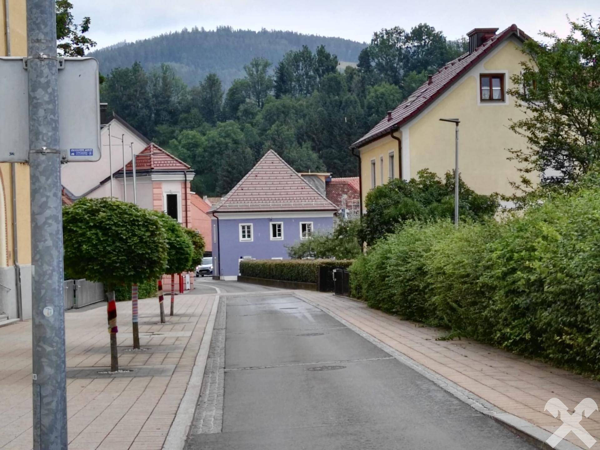 Straße mit dem blauen Gebäude im Hintergrund, umgeben von Bäumen und einem bewaldeten Hügel.