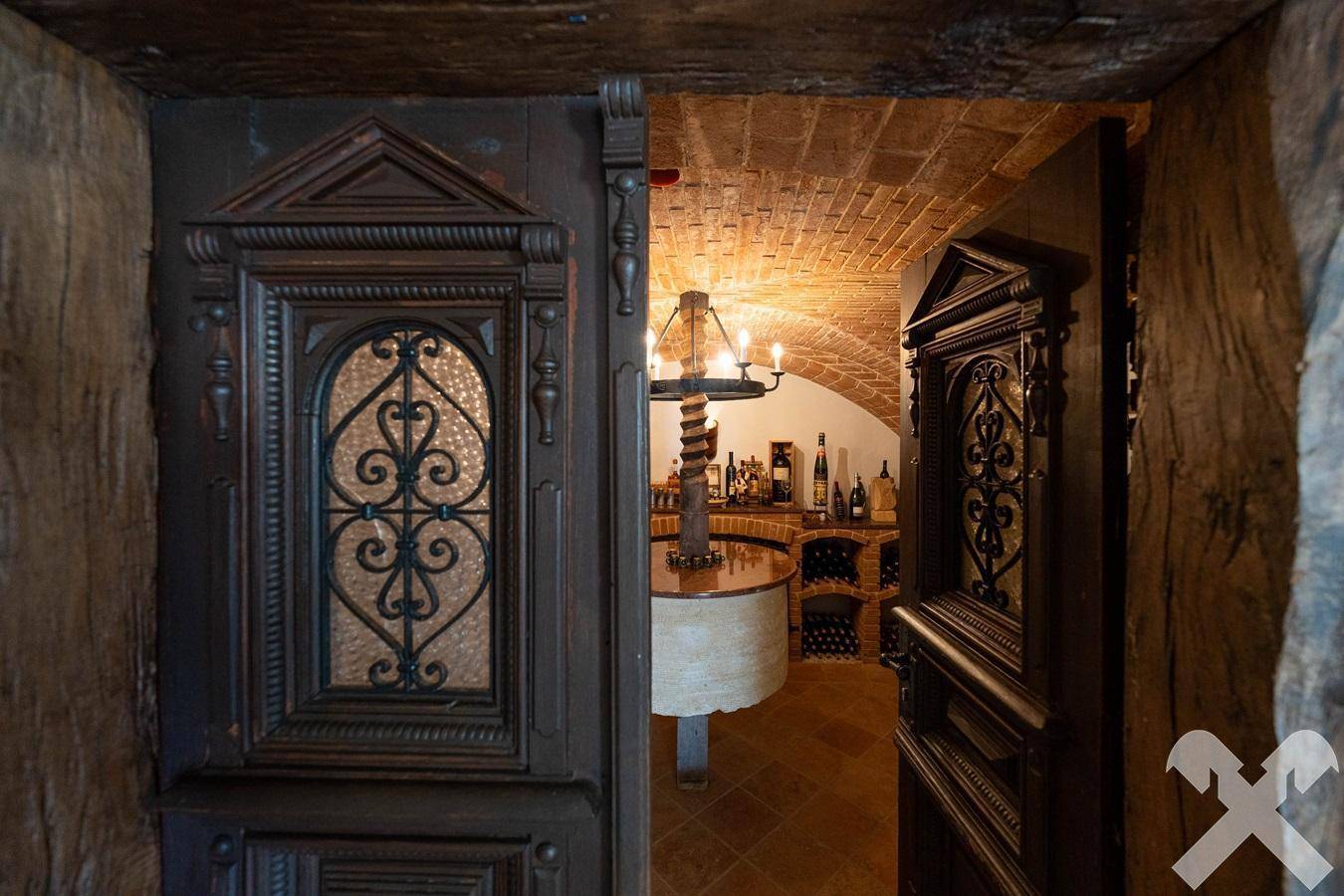 Blick durch eine kunstvoll geschnitzte Holztür in den stimmungsvollen Weinkeller mit Gewölbedecke.