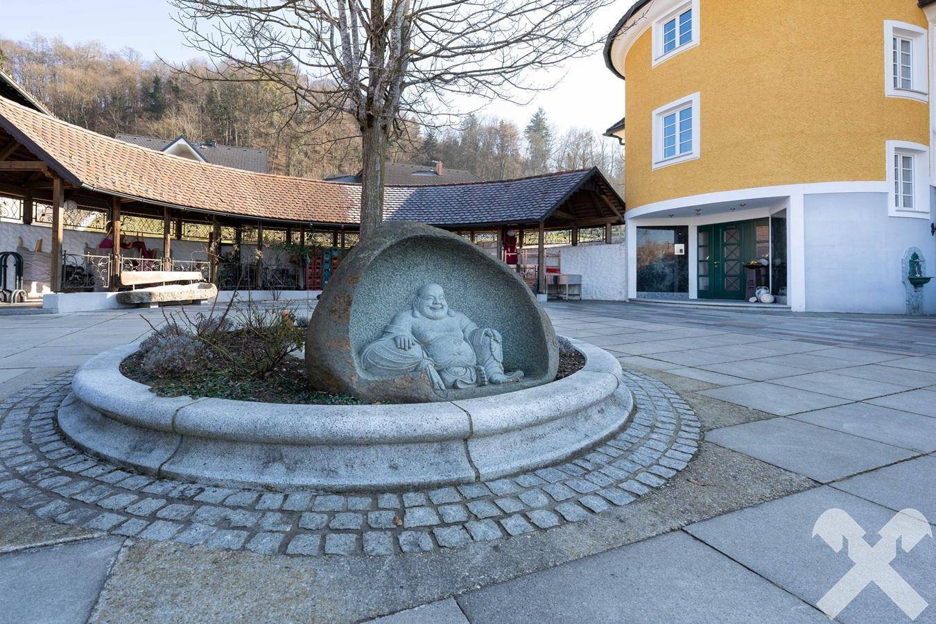 Mediterraner Innenhof mit Buddha-Statue und überdachtem Bereich, umgeben von Gebäuden.