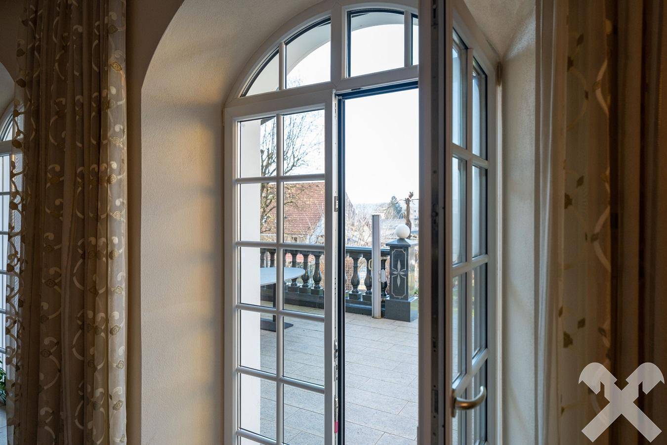 Große Fenstertür führt auf eine Außenterrasse mit Balustrade und weitem Blick.