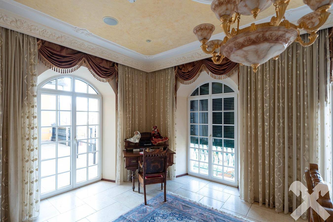 Elegantes Zimmer mit großen Rundbogenfenstern, schweren Vorhängen und Stuckdecke.