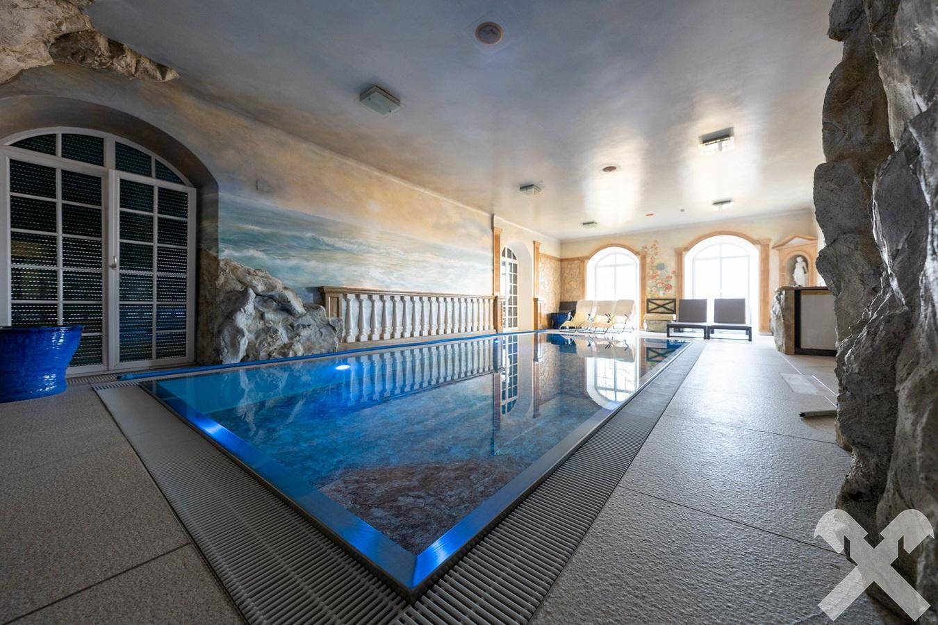 Exklusiver Innenpoolbereich mit Wandmalereien und großen Fenstern für viel Tageslicht.