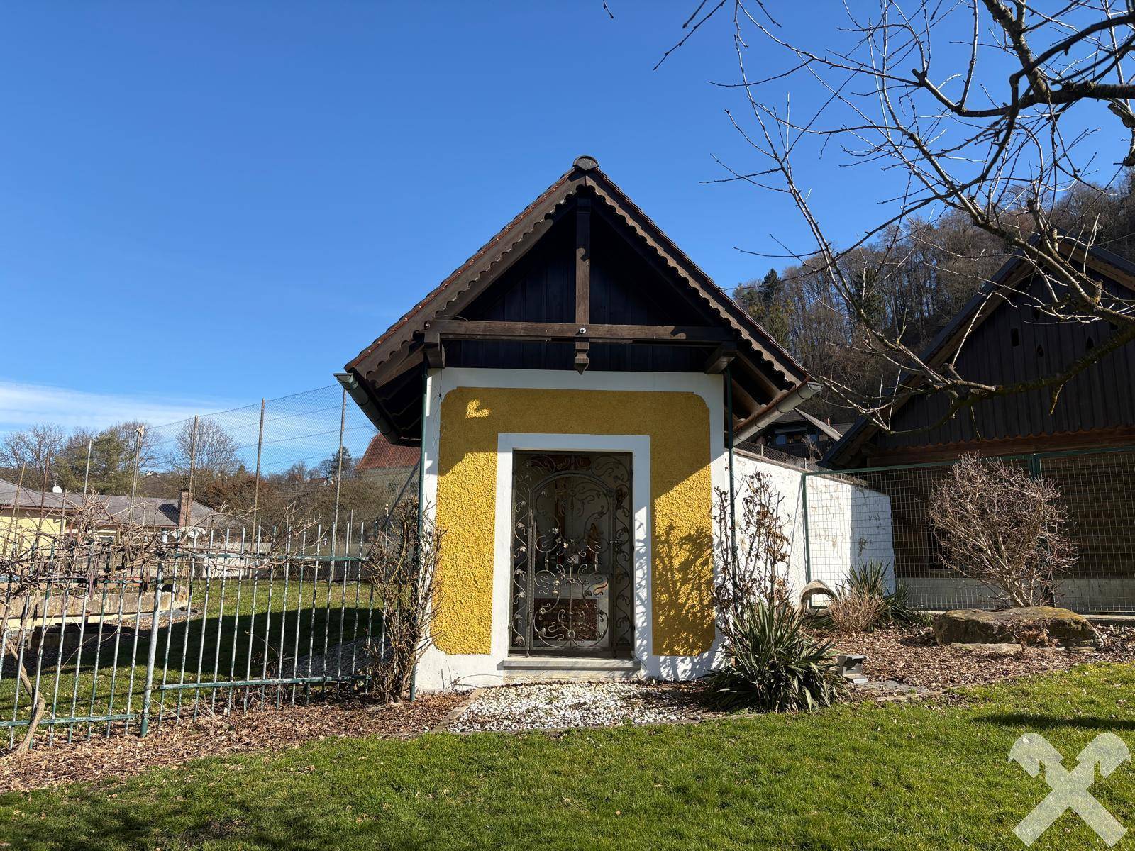 Kleines, charmantes Gebäude mit gelber Fassade und Holzdach, umgeben von Grünflächen.