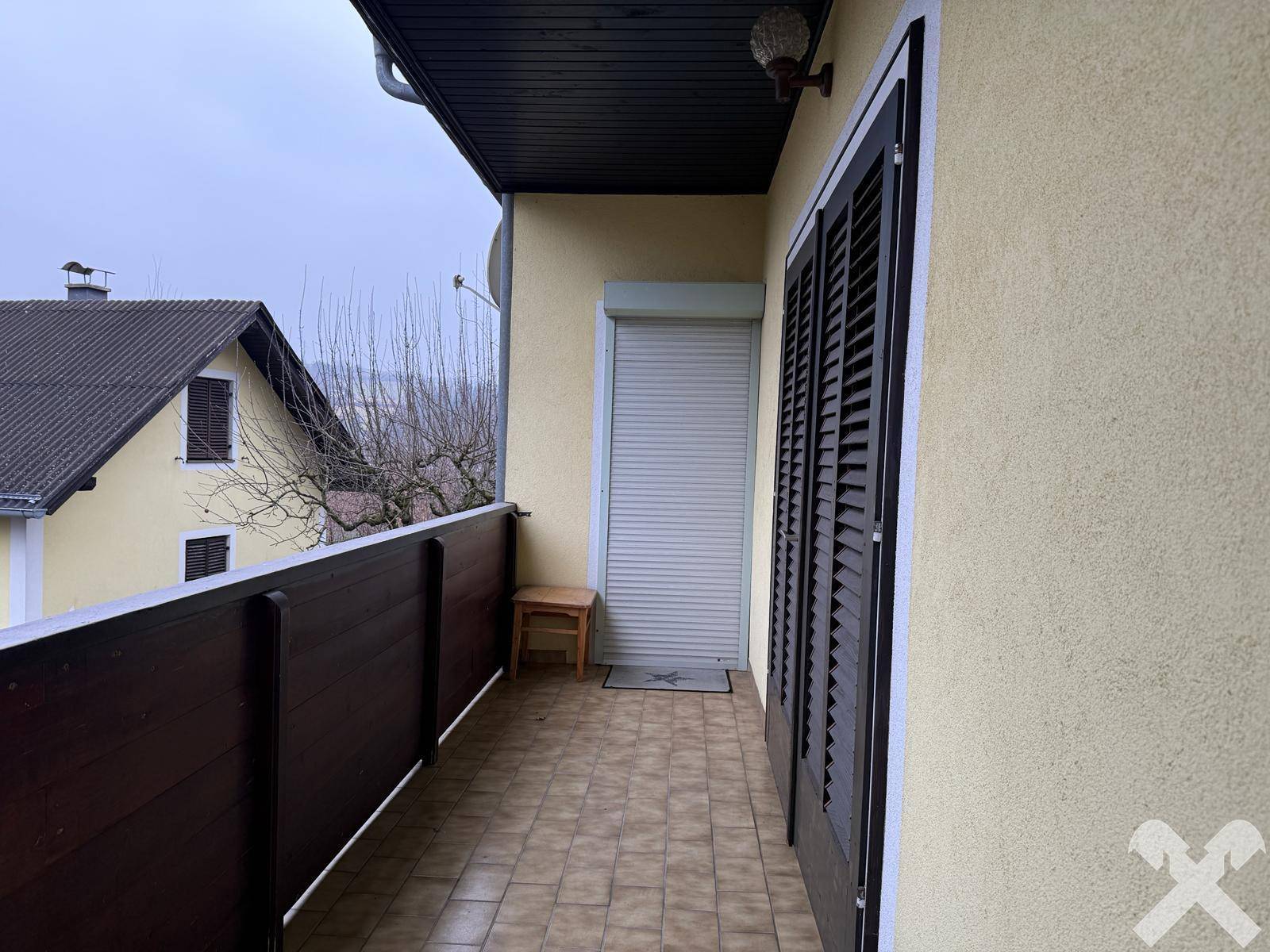 Überdachter Balkon mit Fliesenboden und Holzbalkonbrüstung, ideal für Entspannung.